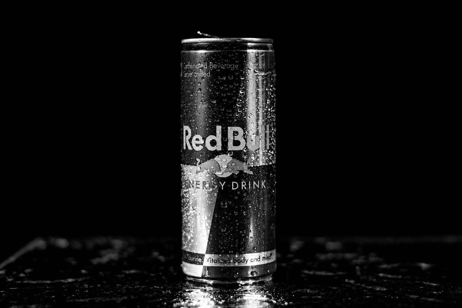 Lata de Red Bull coberta de gotas d'água sobre fundo preto, em preto e branco.