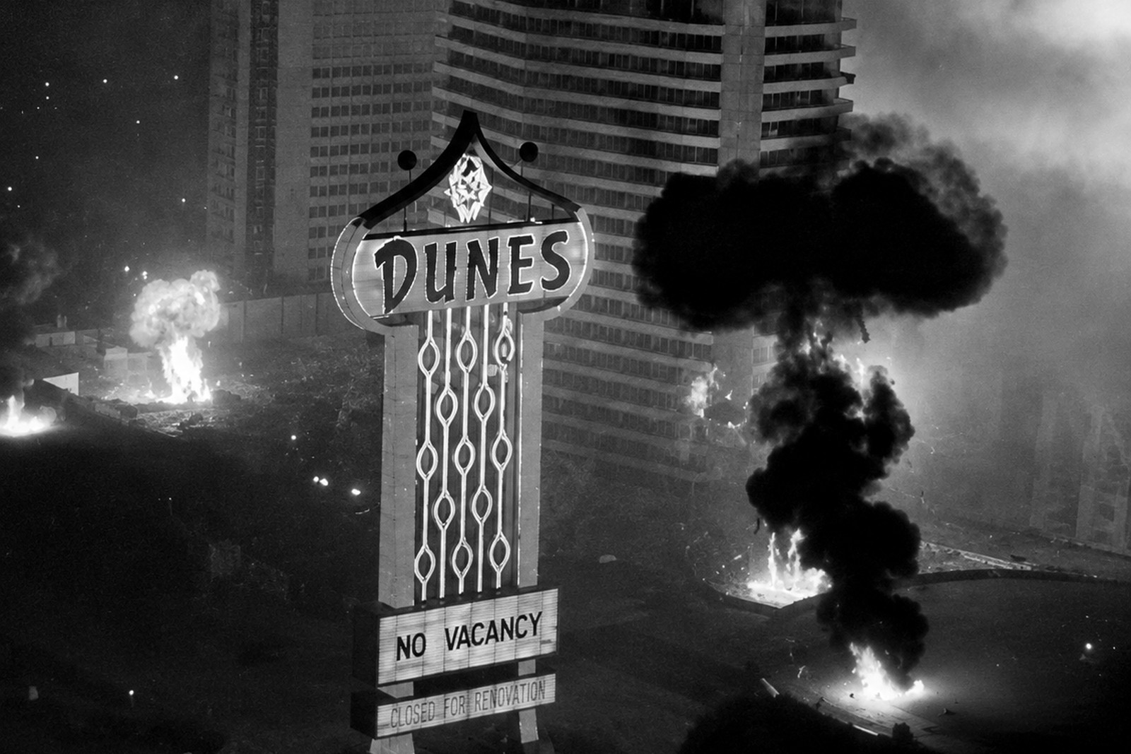 O letreiro do Dunes iluminado, com os dizeres NO VACANCY e CLOSED FOR RENOVATION, diante da torre do hotel em demolição e de uma coluna de fumaça.